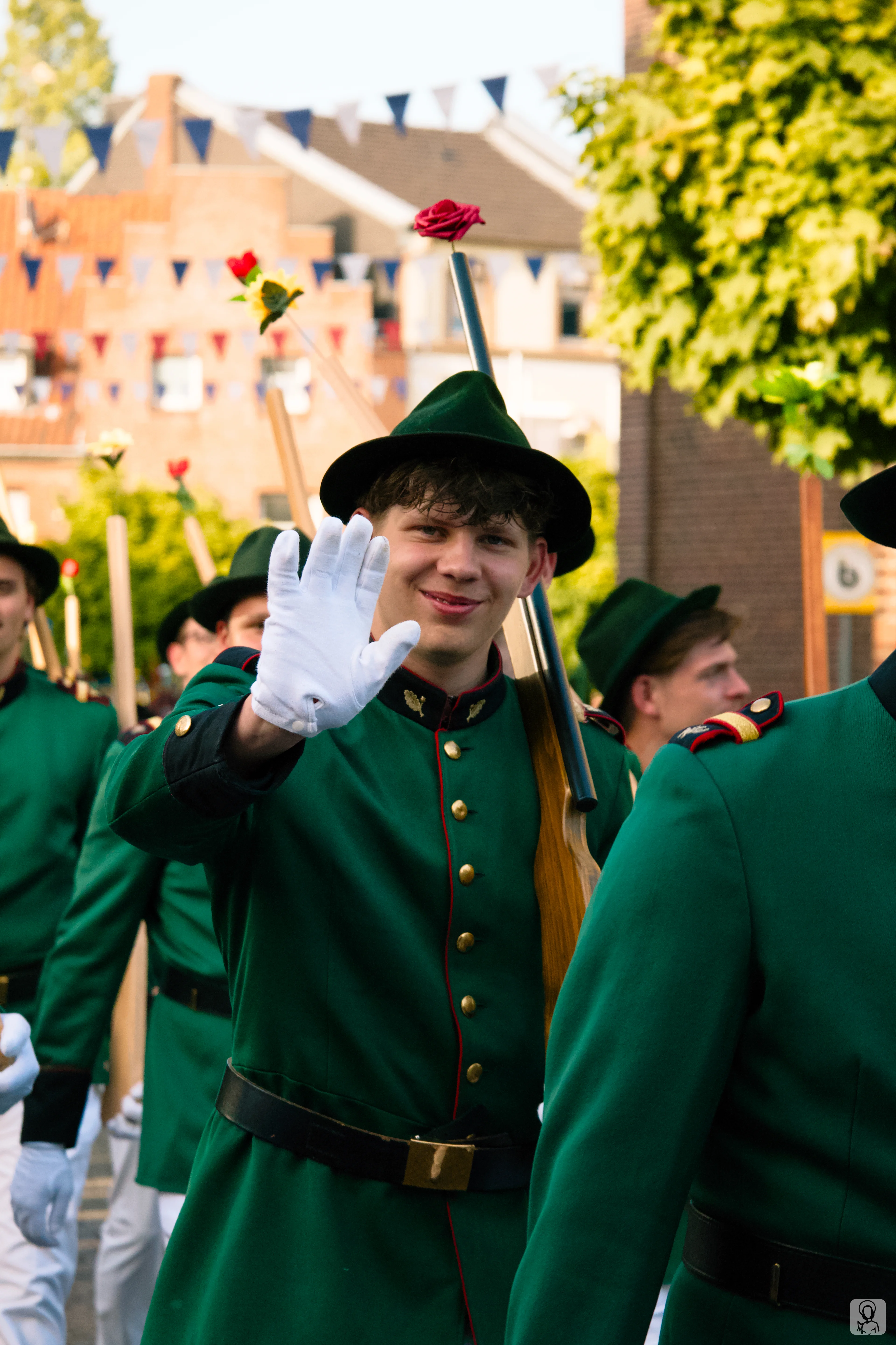 Ein junger Schütze in grüner Uniform und weißen Handschuhen winkt fröhlich lächelnd in die Kamera während eines Festzugs.
